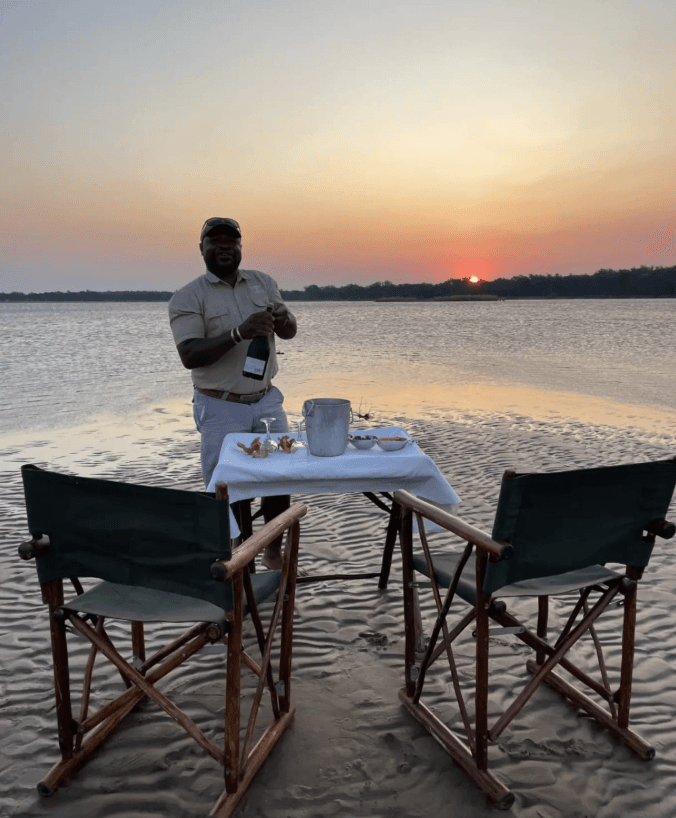 Private sundowner setup on the Zambezi at sunset with a smiling safari guide pouring champagne